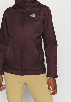 Burgundy North Face jacket with front zipper and logo on chest, worn by person with beige pants and dark skin tone.