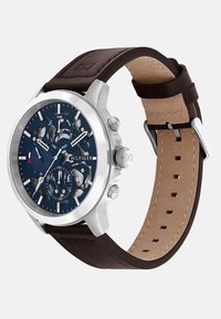 Montre chronographe avec un boîtier en acier inoxydable, cadran bleu marine, bracelet en cuir marron et index et aiguilles en argent.