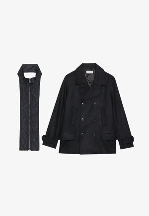 Musta villapaltto, jossa on kaksiriviset napit ja suuri kaulus, yhdistettynä olkaimettomaan mustaan toppaliiviin, joka avautuu vetoketjulla.