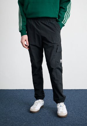 Svarta cargobyxor med elastiskt midjeband, sidofickor och dragkedjedetalj på låret. Matchas med vita sneakers med grå detaljer.