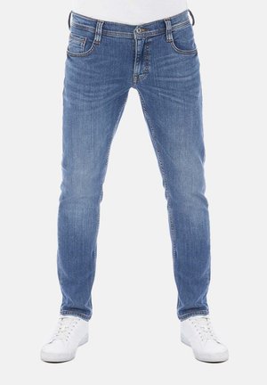 Jeans de mezclilla azul de corte ajustado con cinco bolsillos, costuras en contraste y cierre de botón. Llevados con zapatillas blancas.