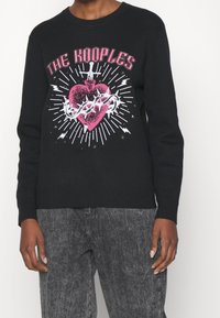 Czarny sweter z kolorową grafiką serca, miecza i cierni, z tekstem "THE KOOPLES" w różowych i białych akcentach. Miękka dzianina.