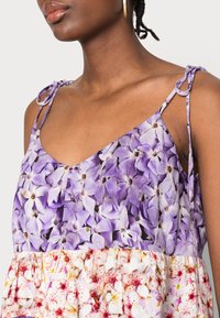 Vestido sin mangas con estampado floral en tonos morados y tirantes ajustables, que presenta un diseño en capas con un patrón floral en colores pasteles en la parte inferior.