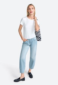 Un haut blanc à manches courtes côtelé associé à un denim droit bleu clair, avec des ourlets retournés, et des mocassins noirs avec des détails texturés.