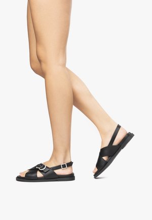 Black leather sandals featuring a flat sole, cross-strap design, and an adjustable buckled ankle strap for secure wear.