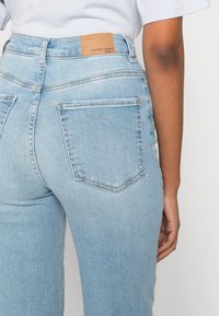 Ljusblå denimjeans med hög midja, bakfickor med sömnadsdetaljer och en läderetikett med texten "perfekta jeans" på midjebandet.