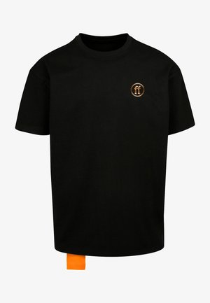 Fekete pamut póló, kis, kerek narancssárga logóval a mellrészen és narancssárga címkével az alsó szegélynél. Rövid ujjú, kerek nyakkivágású.