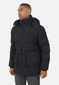 Zwarte pufferjack met een gestructureerde afwerking, hoge kraag en een ritssluiting aan de voorkant. Heeft zijzakken en een capuchon met drukknoopsluitingen.