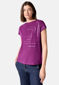 Camiseta de algodón morada de mangas cortas, con un patrón geométrico plateado en la parte frontal, cuello redondo y corte relajado.