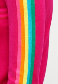 Φωτεινό ροζ ύφασμα με κάθετες πλεκτές ρίγες σε ροζ, πορτοκαλί, κίτρινο, ανοιχτό μπλε και πράσινο σε ένα μανίκι.