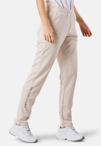 Beiga sweatpants med en smal passform, elastisk midja, sidsömmar och texten "SWEDEMOUNT" tryckt i grått på vänster ben. Bärs tillsammans med vita sneakers.