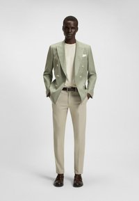 Hellgrüner doppelreihiger Blazer, cremefarbenes Hemd, beigefarbene Hose, dunkelbraune Schuhe. Glatte Textur, taillierte Passform, minimalistisches Design, keine Muster.