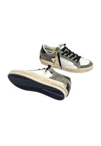 Sneakers in suede grigio e bianco con dettagli neri, superficie texturizzata, suola in gomma piatta, punta perforata e dettaglio con etichetta appesa.