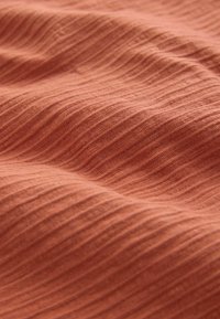 Blødt, ribbet stof i varm terrakottafarve med blide folder, der skaber en tekstureret, bølget overflade.