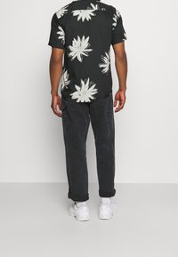 Maglietta nera a maniche corte con motivo floreale bianco, abbinata a pantaloni cargo scuri e sneakers bianche. Design semplice e funzionale.