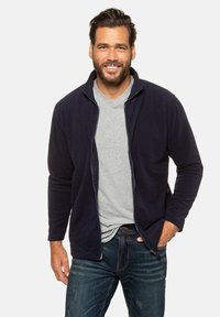 Marine fleece zip-up jack met een grijze V-hals t-shirt eronder. Heeft lange mouwen en zijzakken. Gecombineerd met vervaagde blauwe spijkerbroeken.