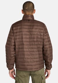 Brun puffjacka med horisontellt kviltat mönster, hög krage och elastiska mudd. Tillverkad av smidigt, lätt material.