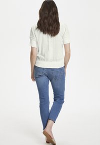 Blusa bianca con texture e maniche corte, abbinata a jeans blu. La blusa presenta un orlo elasticizzato e dettagli in pizzo sulle maniche.
