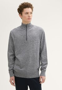 Gray knit sweater with a high collar and a quarter zipper. Features a textured pattern and a small logo on the hem. Casual fit.