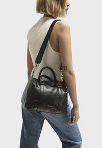 Bolso de mano de cuero negro con doble asa superior y correa de hombro desmontable. Presenta una textura suave y el logo exhibido en la parte frontal.