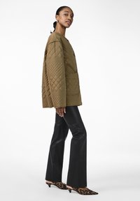 Quilted brown jacket with a relaxed fit, large buttons, and diamond pattern, paired with black flared pants and animal print heels.