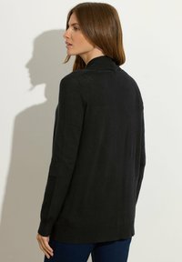 Czarny długi kardigan z długim rękawem, wykonany z miękkiego materiału, z wysokim kołnierzem, prążkowanym wykończeniem i bocznymi rozcięciami dla swobody ruchów.