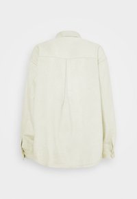 Camicia a maniche lunghe color beige chiaro con una trama morbida, polsini abbottonati e una piega sul retro per un dettaglio di design aggiuntivo. Realizzata in un tessuto confortevole.