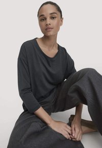 Dunkelgraues, locker sitzendes Langarmshirt mit rundem Ausschnitt, kombiniert mit weit geschnittenen dunklen Jeans. Sanfte Textur, entspannter Stil.