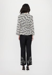 Pantaloni neri a gamba larga con ricami floreali bianchi sull'orlo, abbinati a una blusa a fantasia con linee ondulate nere e bianche.