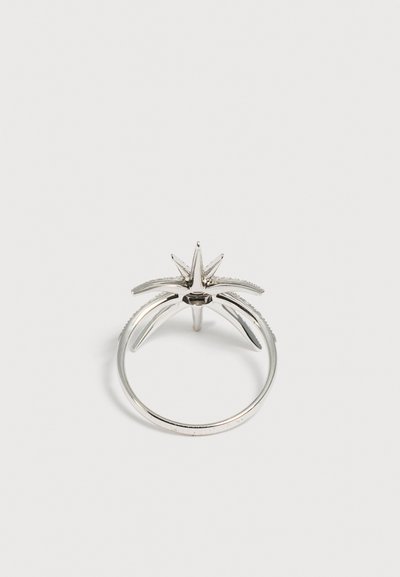 Bague en argent avec un sertissage en forme d'étoile comportant cinq pointes aiguës s'élevant de l'anneau sur un fond blanc uni.