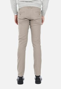 Pantaloni beige slim-fit in cotone con una texture liscia, dotati di due tasche posteriori con chiusura a bottone e aperture delle gambe di lunghezza moderata.