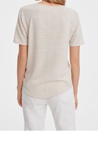 Ljust beige, löst sittande t-shirt med korta ärmar, rundad fåll och textilstruktur, sedd bakifrån.