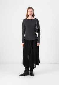 Pilkas ilgomis rankovėmis marškinėliai su apvalia iškirpte, derinami su plačia juoda sijonu ir juodais aukštakulniais batais iki kelių. Ant peties pakabinama maža juoda rankinė.