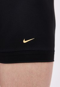 Gros plan sur la partie supérieure de la jambe d'une personne portant un short de sport noir avec un petit logo Nike Swoosh doré près de l'ourlet.