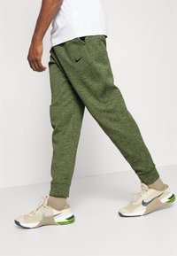 Joggers verdes e texturizados com punhos elásticos e bolsos laterais. Combinados com sapatilhas bege e cinzas, apresentando um logótipo refletor e detalhes verdes.