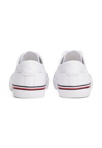 Bílé boty s hladkým syntetickým materiálem, nízkým designem a kulatou špičkou. Obsahují červené a černé akcenty na podrážce.