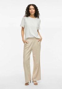 Top gris claro con mangas cortas de encaje bordado, combinado con pantalones de pierna ancha crema y sandalias de tacón ligero beige.