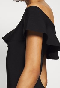 Top nero off-the-shoulder con maniche a volantino, design aderente e dettagli laterali aperti, realizzato in un tessuto liscio ed elasticizzato.