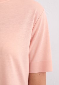Top à manches courtes en tissu doux de couleur rose clair. Il présente un col rond avec des accents côtelés et une texture lisse.