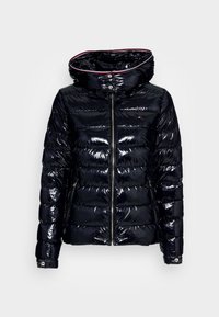 Błyszcząca czarna pikowana kurtka z wysokim kołnierzem, zamkiem z przodu, detalami na zatrzaski i czerwoną podszewką wewnątrz kołnierza.