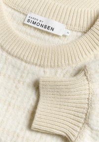 Sweter w kolorze off-white z teksturowanym wzorem dzianiny, ściągacze przy kołnierzu i mankietach, oraz markowa metka "KAREN BY SIMONSEN" w kolorze czarnym, rozmiar M.