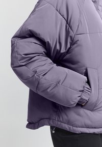 Giacca a vento viola con design trapuntato, presenta maniche ampie, polsini elasticizzati e tasche laterali, realizzata in materiale leggero e morbido.