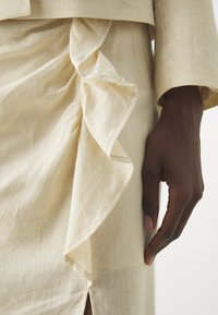 Beige pellavamekko, jossa on frilla-detail sivussa ja halkio. Sujuva tekstuuri, jossa on yksinkertainen kaula-aukko ja hihasuunnittelu.