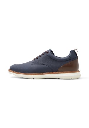 Zapato casual para hombre en azul marino y marrón con cordones, suela blanca, perfil bajo y collar acolchado, mostrado de perfil.