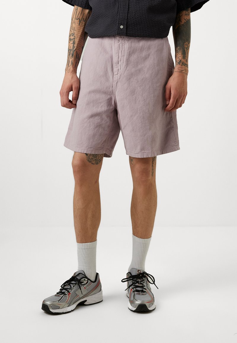 Lyse lilla shorts laget av teksturert stoff, med en avslappet passform og et enkelt design. Båret med grå sneakers og hvite sokker.