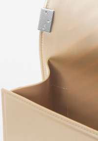 Sac à main beige avec un extérieur lisse, doté d'une fermeture à clip en argent, et d'un intérieur spacieux au design minimaliste.