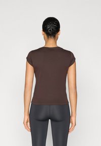 Brown fitted t-shirt with short sleeves, smooth fabric, round neckline, and a subtle stretch, worn with dark leggings.