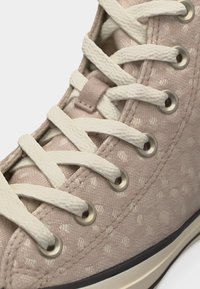 Αθλητικό παπούτσι από ανοιχτό ροζ ύφασμα με λευκά κορδόνια που περνούν μέσα από ασημένιες θηλιές και διακριτικό πουά μοτίβο.