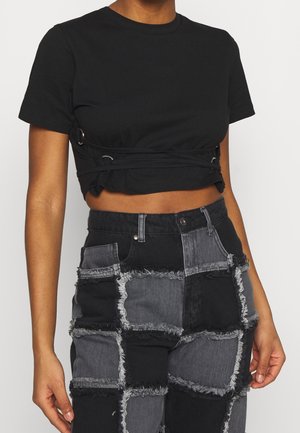 T-shirt noir court en coton, avec un design noué et des accents de quincaillerie argentée sur le côté, accompagné d'un pantalon en denim noir patchwork.