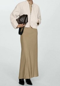 Light quilted bomber jacket in cream, paired with a beige fitted maxi dress and black ankle boots. Holding a dark brown bag.